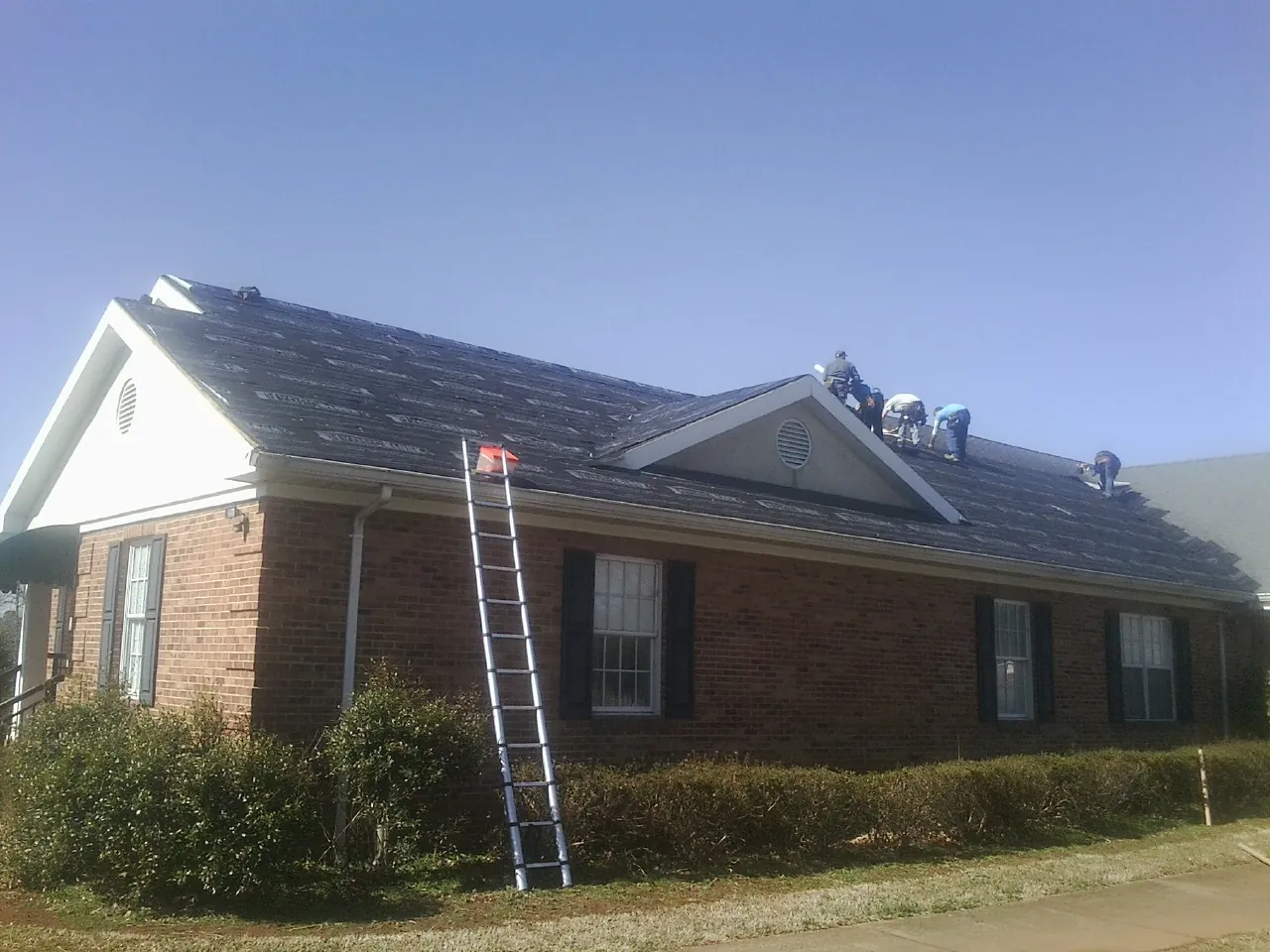 Crew tearing shingles off a brick ranch roof with a ladder set — Emergency Roof Repair work by our crew in Ralph