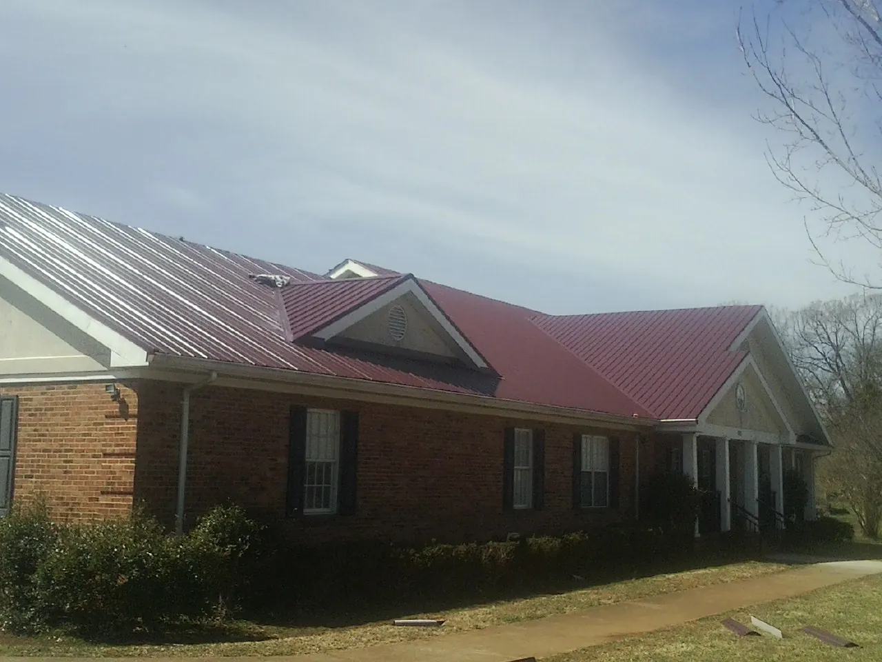 Red metal roof with gabled entries on a long brick building, from a Hail Damage Roof Repair job in Ralph