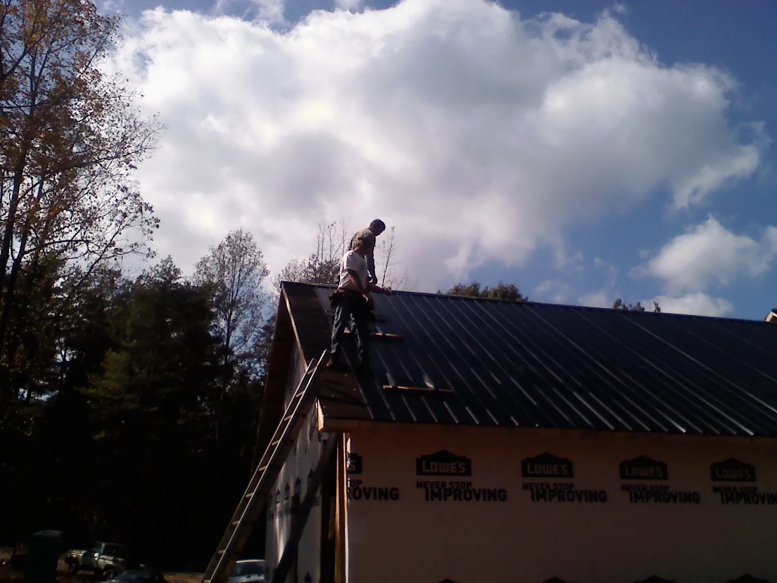 Roofer fastening dark metal panels high against a cloudy sky, from a Roof Inspection job in Ralph